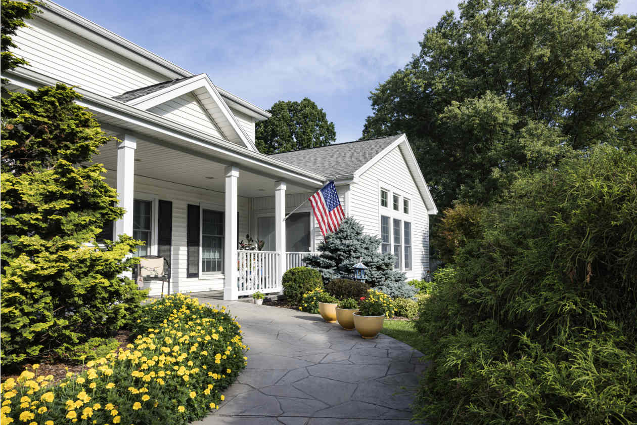 A white house with American flag and flower bed.
