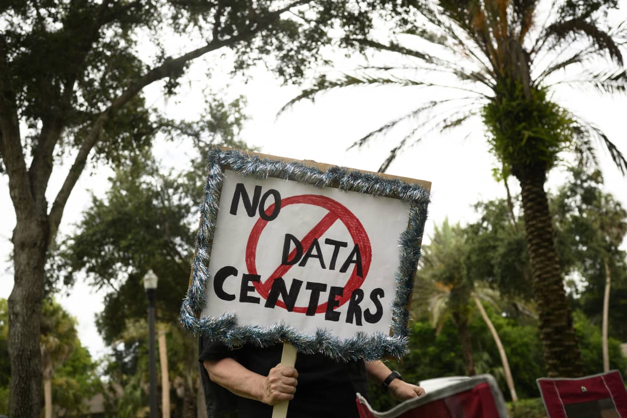 A person holding a sign that reads "NO DATA CENTERS" with "DATA CENTERS" crossed out in a red circle.