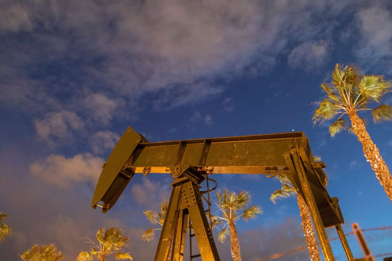 Pump jacks at Long Beach Oil Field under a night sky with palm trees.