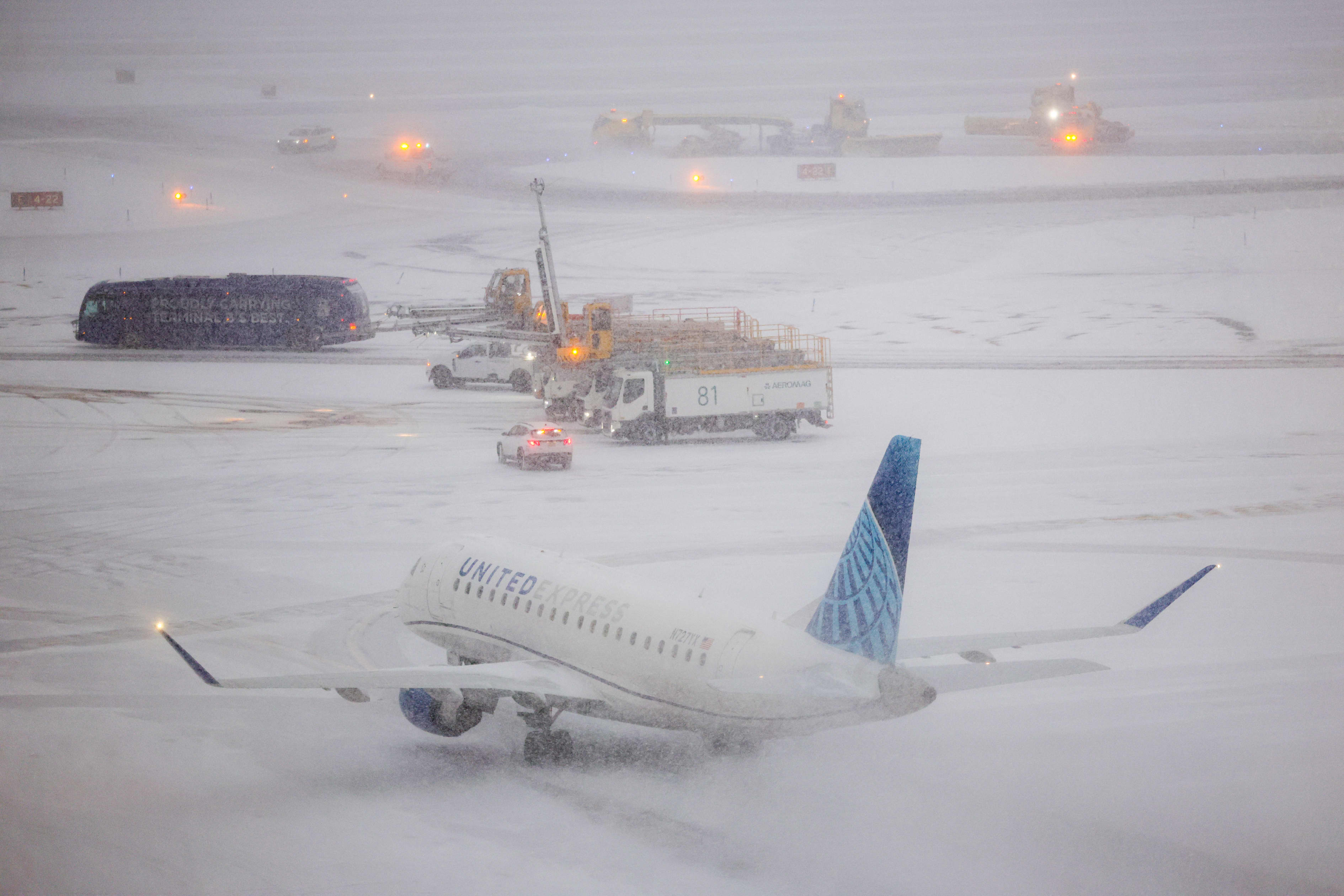A United Express plane and airport service vehicles on a snow-covered airfield during a snowstorm.