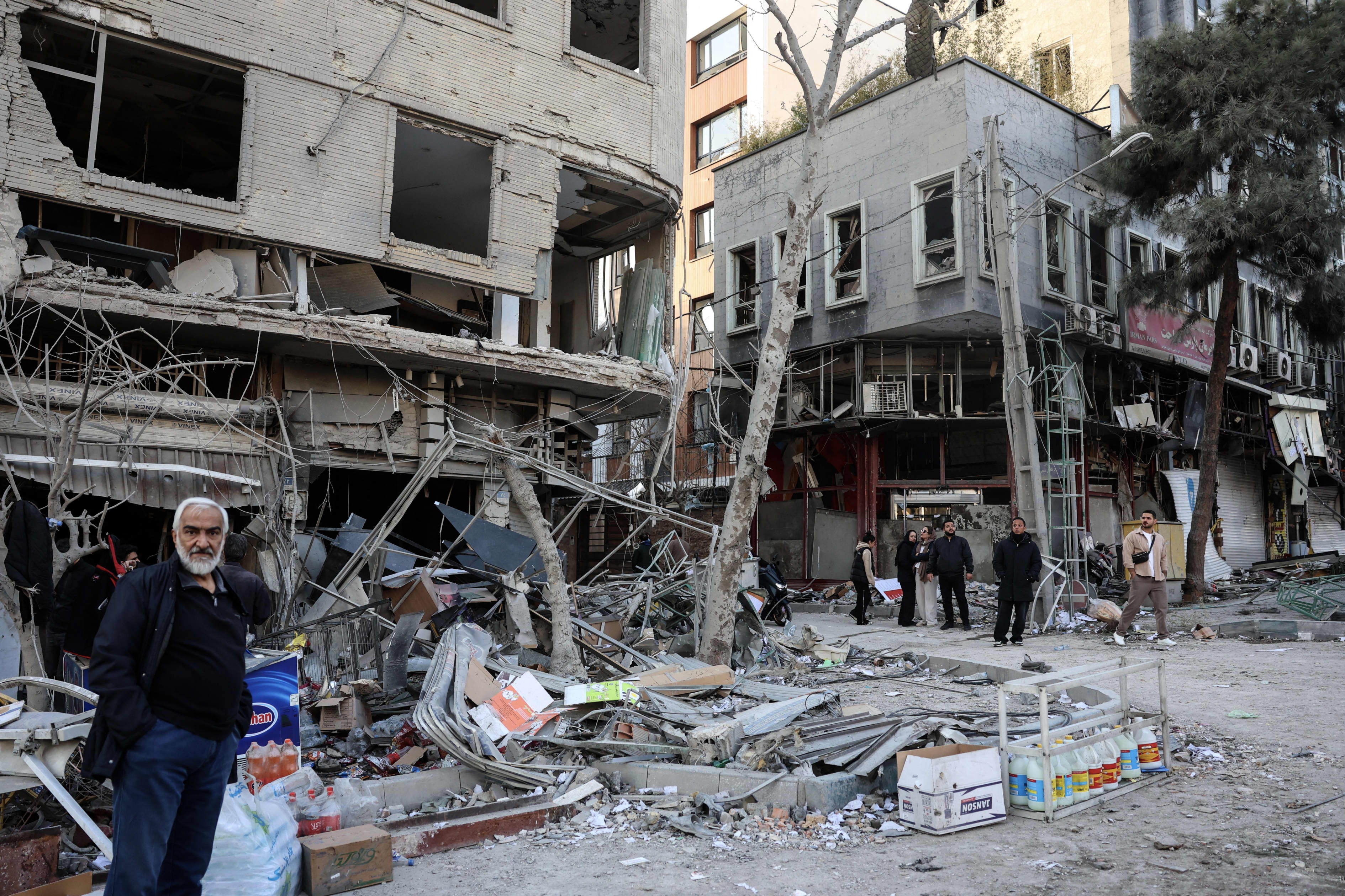 Residents stand on a street near damaged residential buildings in Tehran after an ongoing joint US-Israeli military campaign.