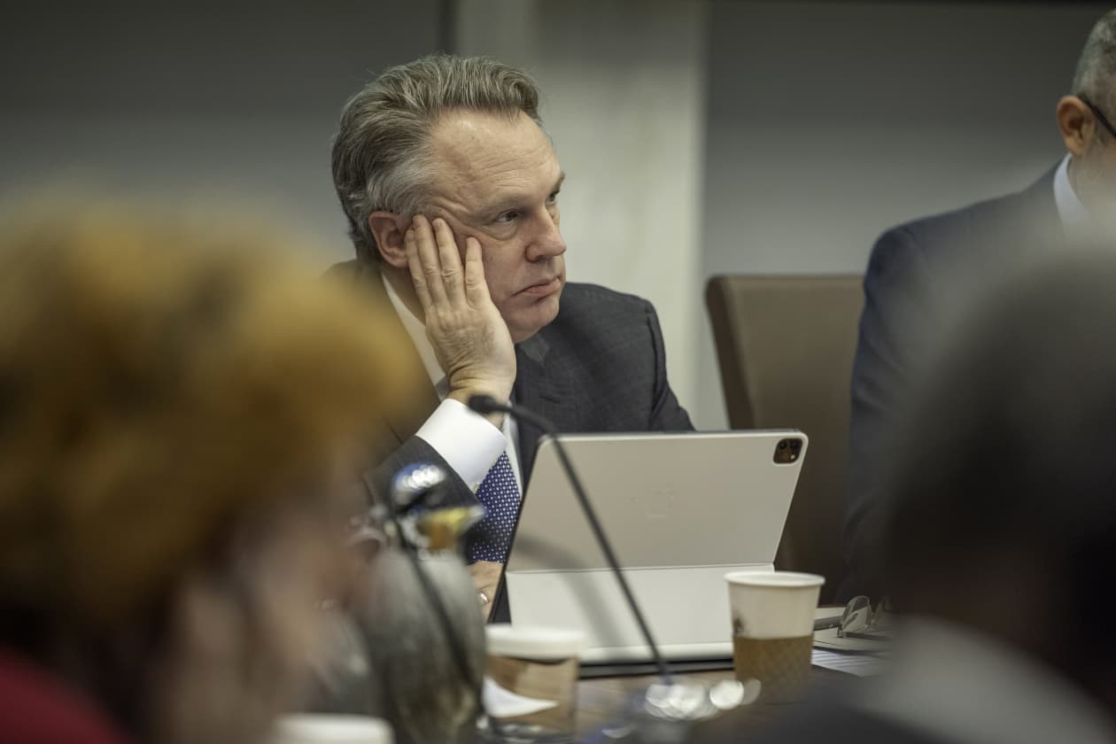 Image 4: A man in a suit rests his chin on his hand, looking pensive during a meeting.