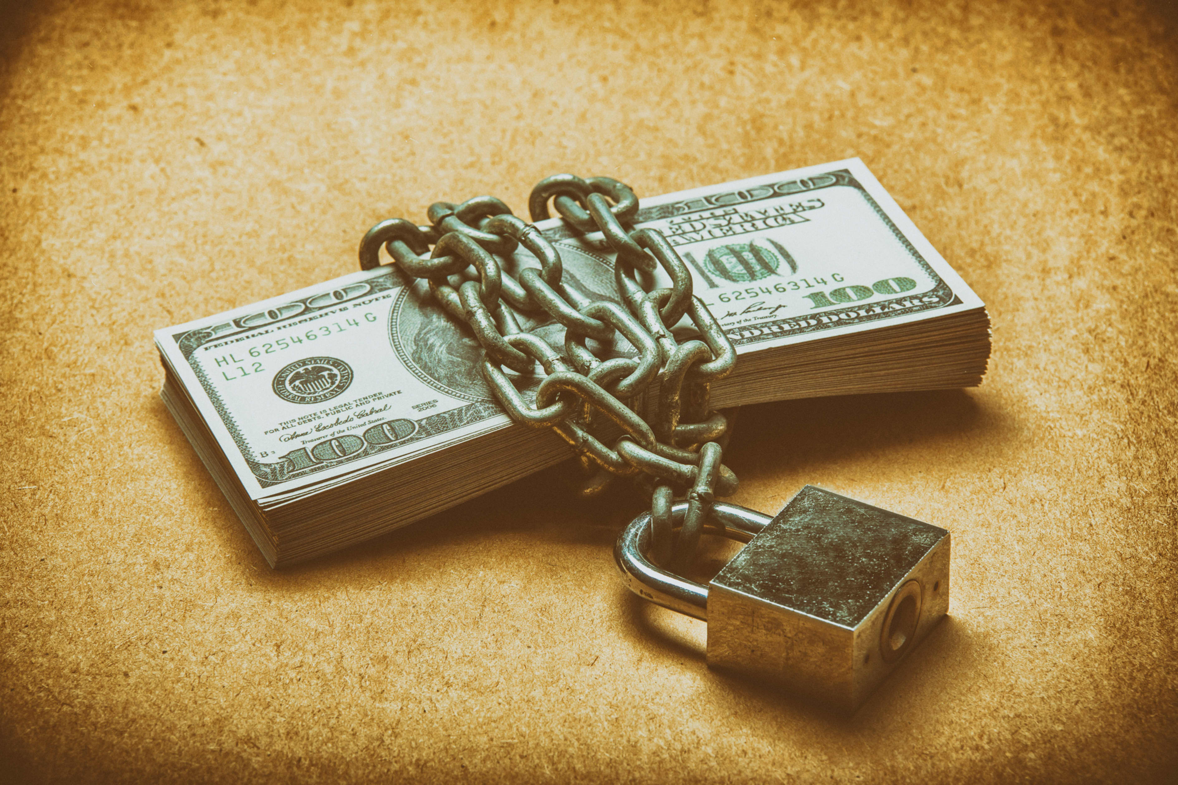 A stack of hundred-dollar bills bound by a heavy metal chain and secured with a padlock.