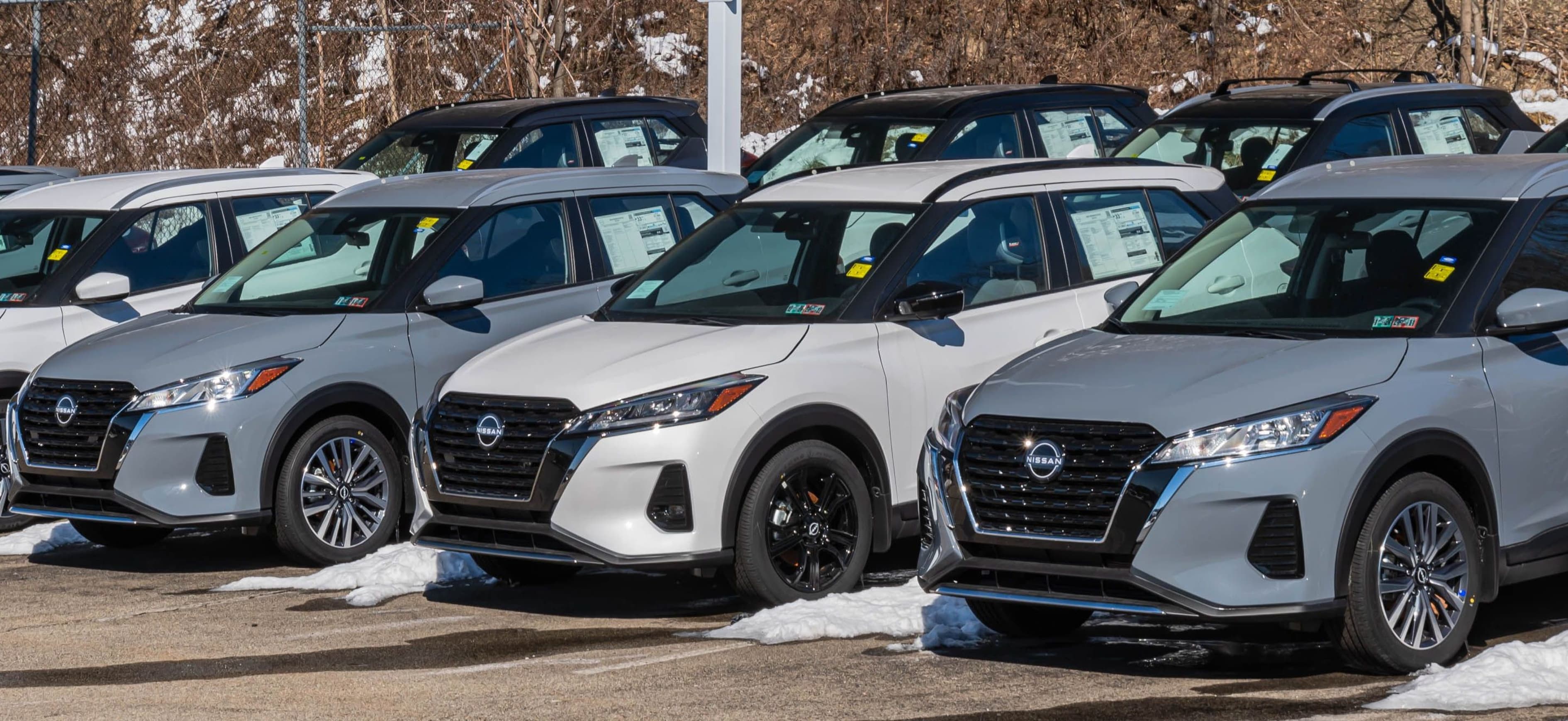A line of new Nissan vehicles for sale at a dealership on a sunny winter day.