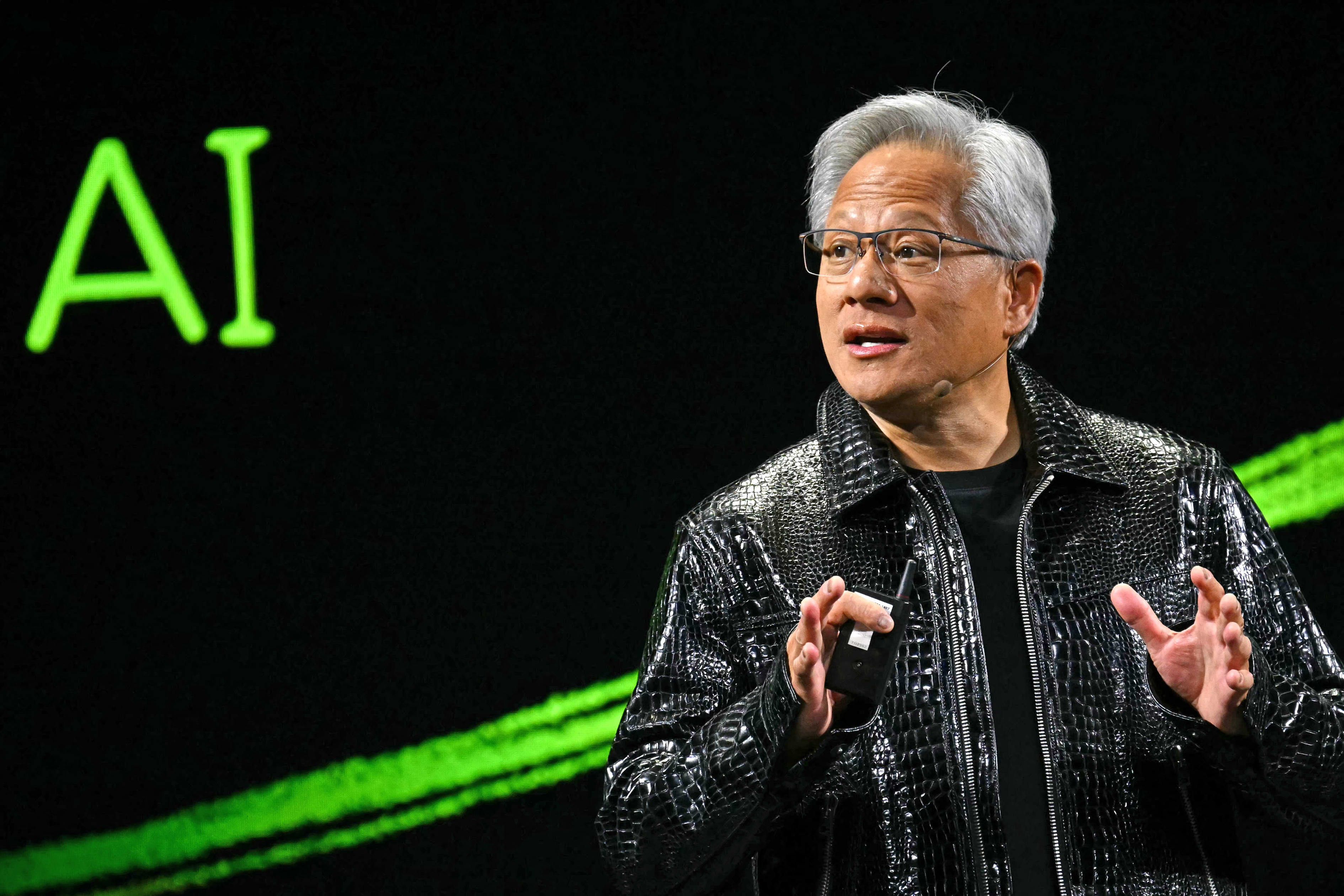 Nvidia CEO Jensen Huang delivering a keynote address with "AI" lit up behind him.
