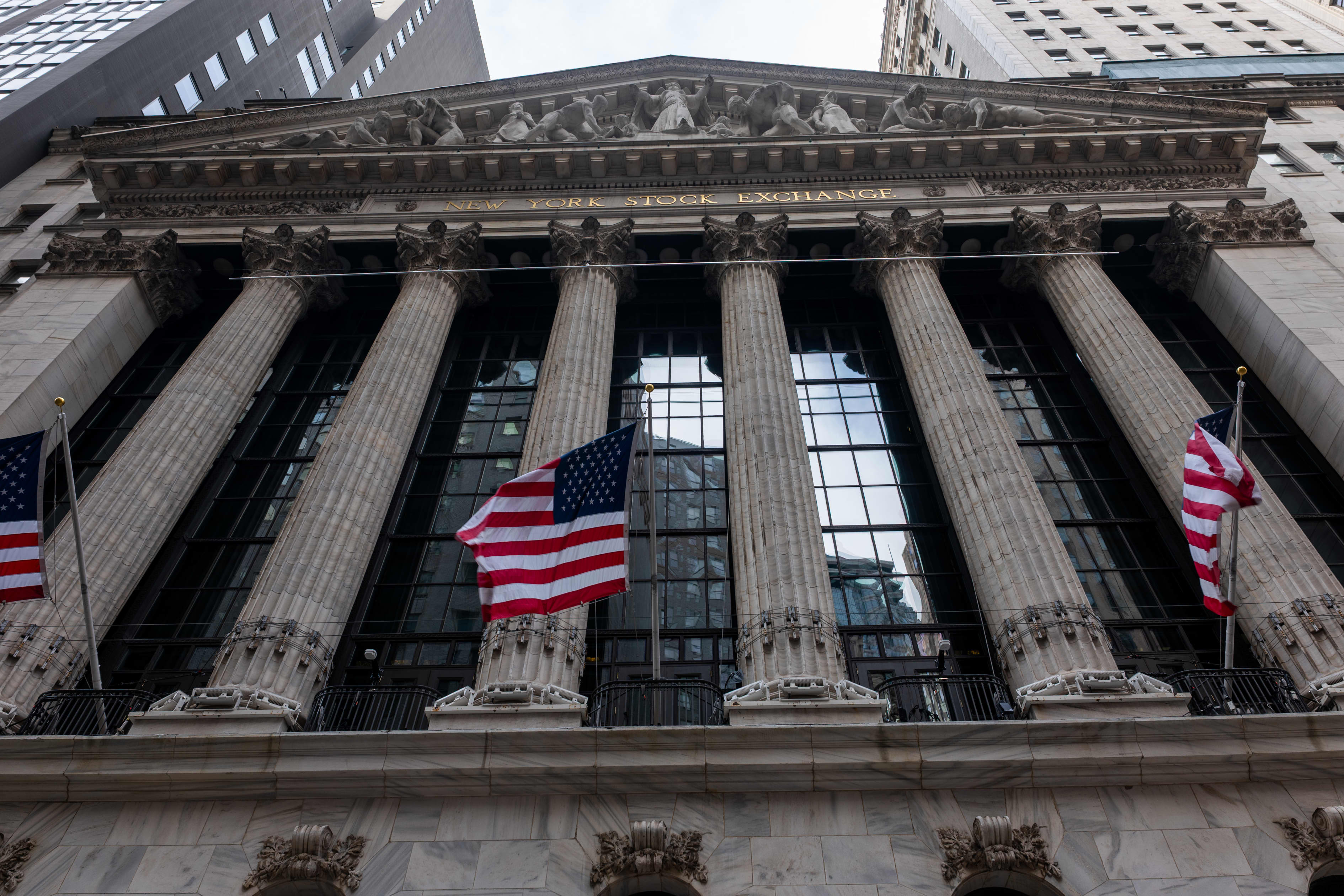 The facade of the New York Stock Exchange building with large columns and American flags flying.