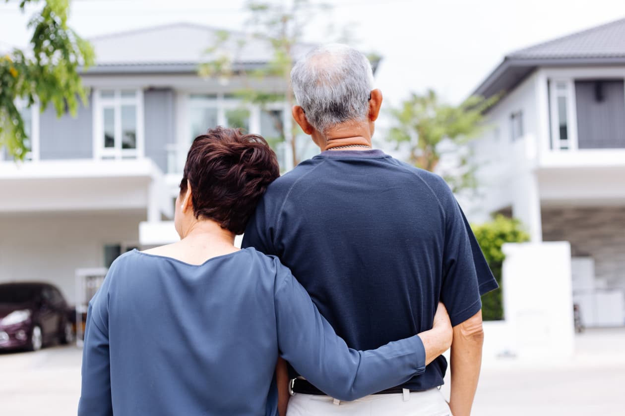 Senior couple from behind looking at their home and car.
