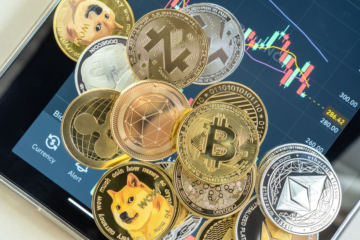 Các loại tiền điện tử bao gồm Bitcoin, Dogecoin, Ethereum và Cardano trên điện thoại thông minh hiển thị ứng dụng giao dịch có biểu đồ nến.