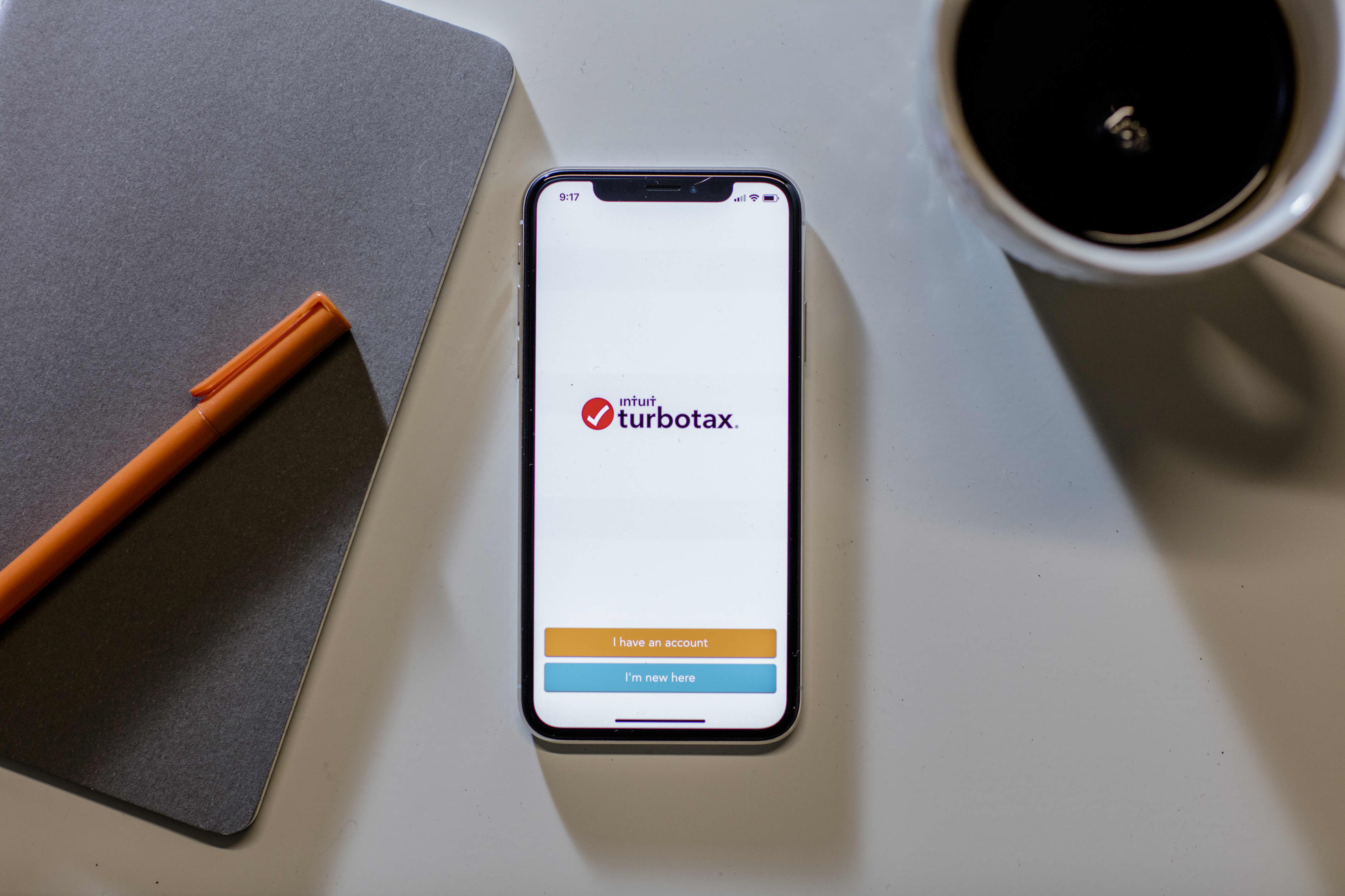 A phone displaying the TurboTax app, next to a notebook, pen and coffee mug.