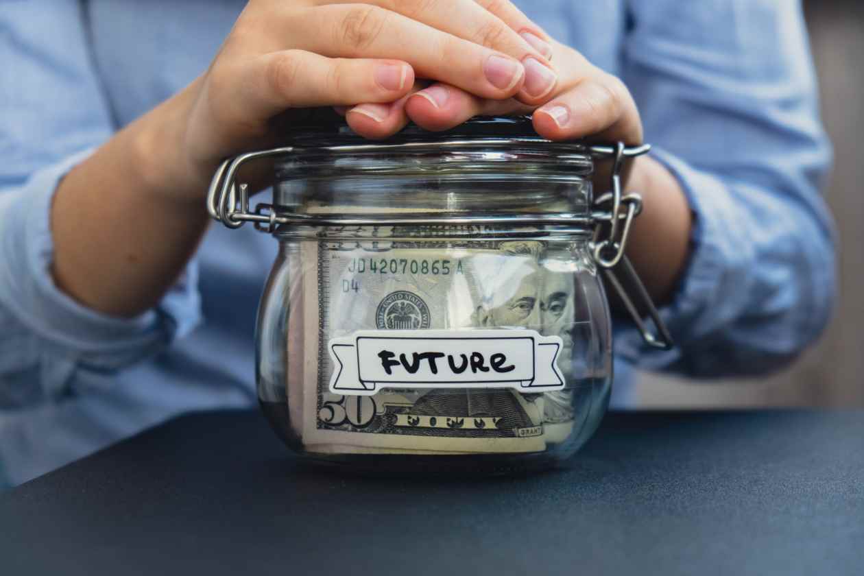 Hands holding a glass jar filled with money and labeled FUTURE.